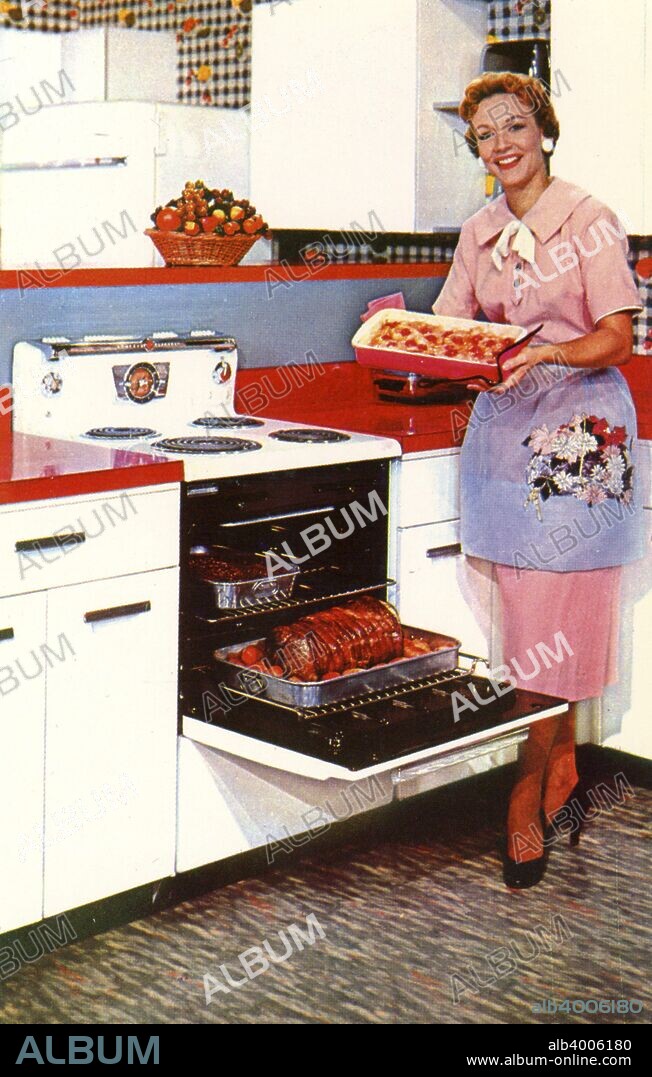 Here's General Electric's Compact Spacemaker oven, USA, 1955. A woman in a shirtwaist dress, high heels and apron in a kitchen. She is showing off a meal cooked in the oven.