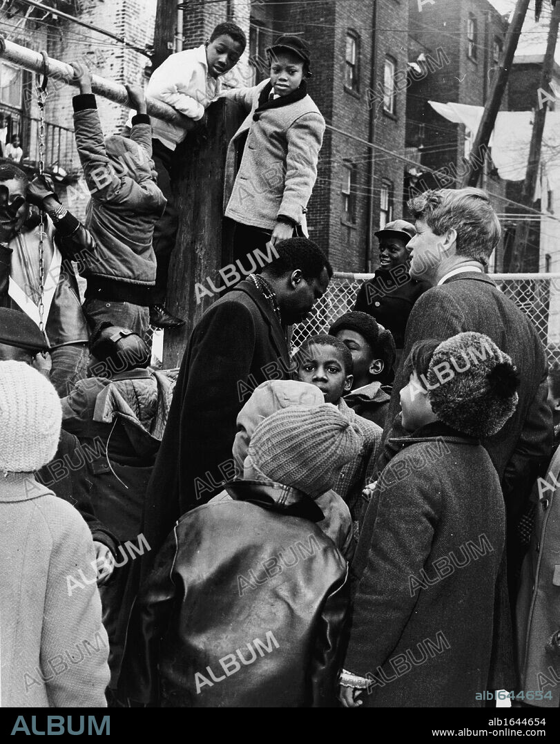 Robert F Kennedy (1925-1968) Democratic Senator for New York, right centre, and Donald F Benjamin. center, of the Central Brooklyn Coordinating Council, join children at playground children outside a building, 5 February 1966. 'World Telegram & Sun' photograph by Dick DeMarsico.