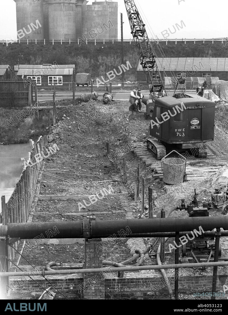 Construction of the reservoir, Manvers Main Colliery, Wath upon Dearne, South Yorkshire, 1955. A Priestman tracked crane at work during the construction of the reservoir at the colliery, near Rotherham. Priestman Brothers were based in Hull. The company was founded in 1870 by William Dent Priestman. The company began the manufacture of construction equipment in 1876 when they were asked to construct machinery to recover lost gold from the sea off the west coast of Spain. No gold was found but the company's equipment proved useful for dredging of harbours and docks. After many acquisitions, the company eventually merged with Coles Cranes of Sunderland, and began building offshore cranes for North Sea oil rig platforms. The company now trades in Bradford under its new owner, Gardner Denver, an American based compressor and blower manufacturer. What is left of Priestman no longer manufactures cranes or excavators.