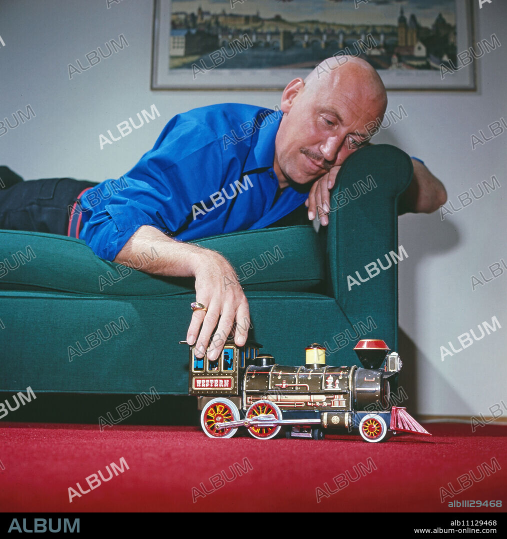 Karl Lieffen, German stage, television and film actor, lying on the couch and playing with a small steam locomotive, Germany around 1979. (original german headline: Karl Lieffen).