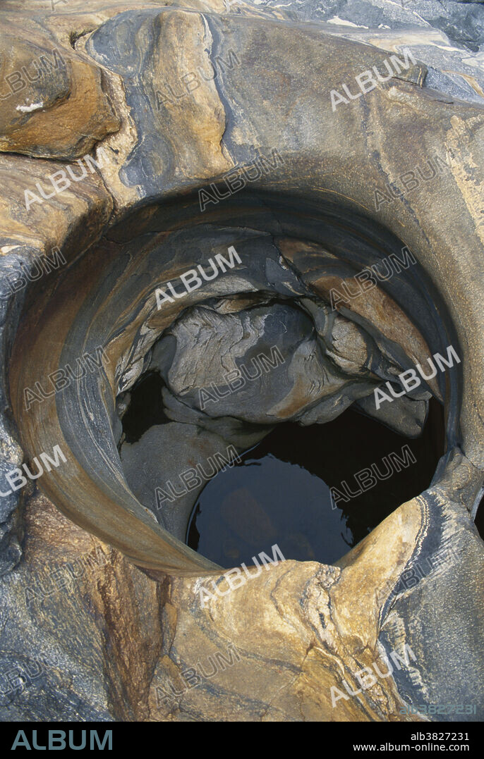 Glacial pothole in granite with many mineral streaks; Shelburne, Massachusetts. Potholes most commonly occur in areas where there are ancient rocks with different resistances to erosion. Stronger pebbles fall into small cavities in stream bottoms and swirl, widening and deepening the cavities.