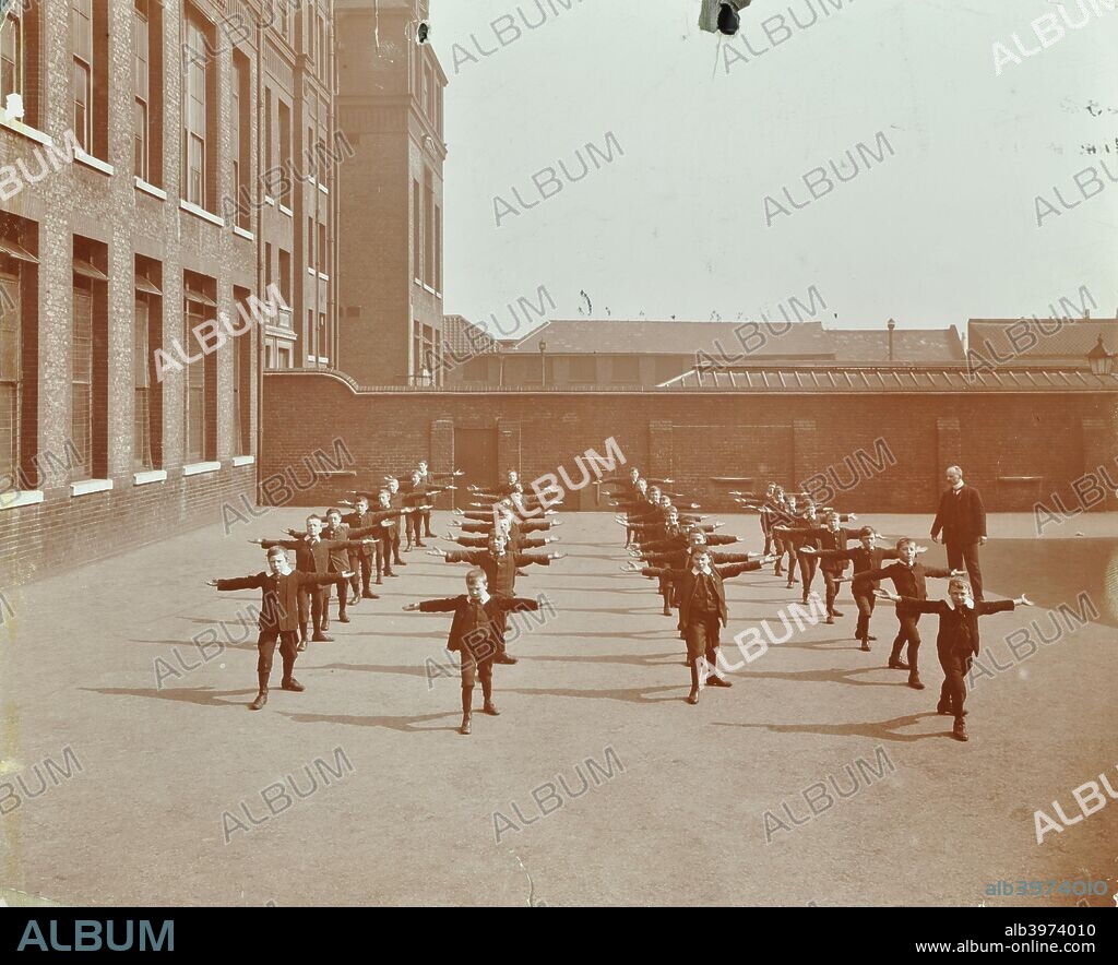 Drill in playground, Alma Boys School, Bermondsey, London, 1908. A class of boys, all with their arms outstretched, undergo an exercise drill under the instruction of a teacher.