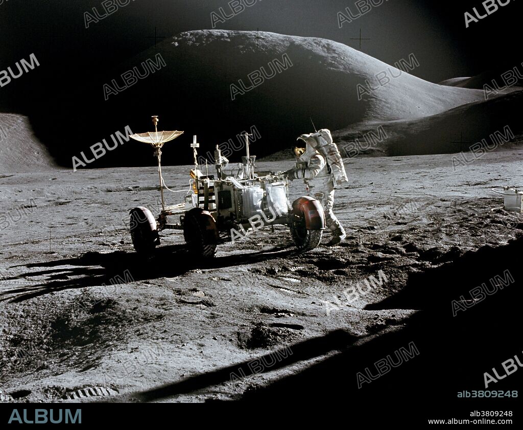 Astronaut James B. Irwin, lunar module pilot, works at the Lunar Roving Vehicle during the first Apollo 15 lunar surface extravehicular activity (EVA) at the Hadley-Apennine landing site on July 31, 1971. The shadow of the Lunar Module "Falcon" is in the foreground. This view is looking northeast, with Mount Hadley in the background. This photograph was taken by astronaut David R. Scott, commander.