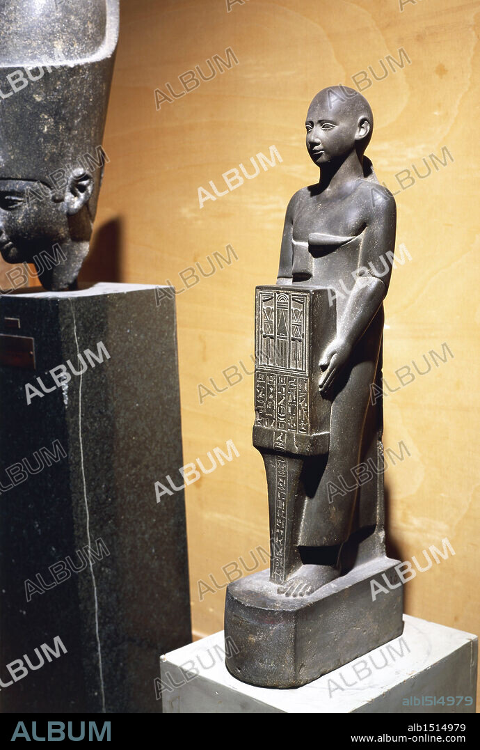 Egyptian civilization, Late Period, Dynasty XXVII. Statue of the priest Henat wearing a Persian robe and holding a tabernacle depicting facade of the temple of goddess Neith at Sais.