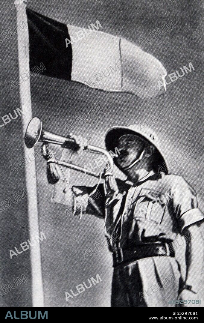 Black and white photograph of World War II (1939-1945); a soldier from the Free French forces in Syria blows on a trumpet with the French flag flying behind him on a flagpole.