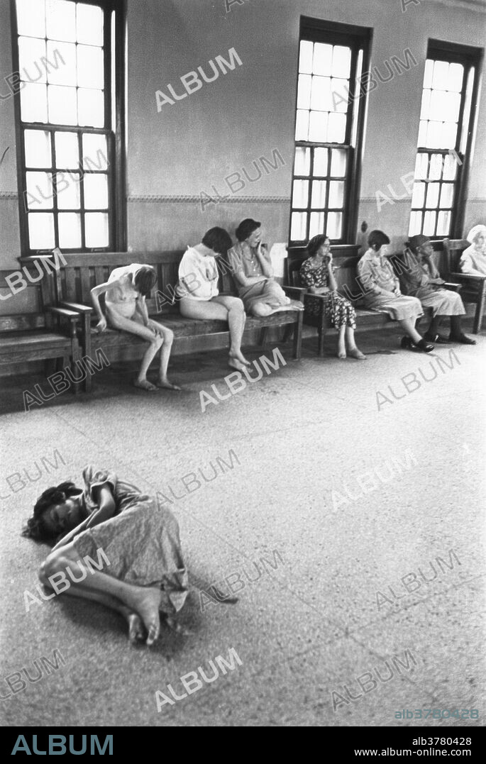 Female patients sitting in a common room of the Ohio Insane Asylum while one patient lies on the floor, 1946.