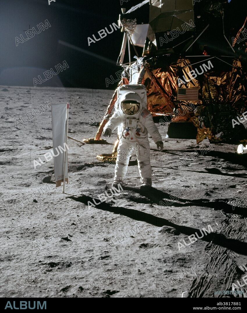 Apollo 11 astronauts Neil Armstrong and Edwin "Buzz" Aldrin performed the first manned lunar landing on 20 July, 1969. This photo shows Buzz deploying the SWC. The photo is taken toward the southeast. Buzz is standing flat-footed next to the Solar Wind Collector, (SWC) facing Neil who is at about the 2 o'clock position out from the Lunar Module. In the lower right corner, notice the tracks that the TV cable made as Neil pulled it out. The multiple tracks were made by the individual cable loops scraping along the ground. We can see under the engine bell. Most of the surface in this image has not yet been disturbed, and in the places where Neil and Buzz have walked, the disturbed surface is darker. Good illustration of this very common phenomenon. Jack Schmitt speculates that the Descent Engine plume swept away the smallest particles, leaving a higher than normal percentage of larger particles. The more jagged surface is a better reflector of sunlight than the normal surface and, therefore, appears brighter. Certainly, from orbit, the areas around the landed LM's are brighter than the normal surface. As they walk around, the astronauts disturb this modified surface and, in effect, restore its normal condition.