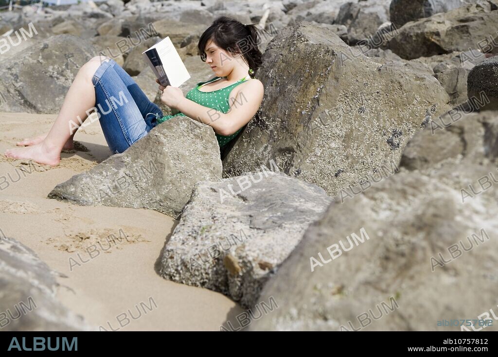 Seventeen year old girl reading at beach.