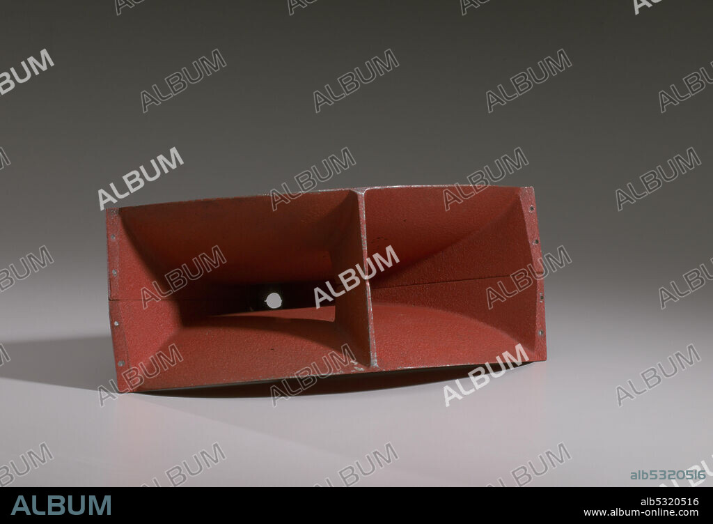 A Cerwin-Vega horn speaker. The speaker front is rectangular in shape and painted orange. The sides of the front concave in towards the middle to create a cone shape. The front also has a bar in the middle of the speaker that splits it into two chambers. The back of the speaker is silver in color and shapes into a conical point. The point splits into two halves that end in a round open circle.
