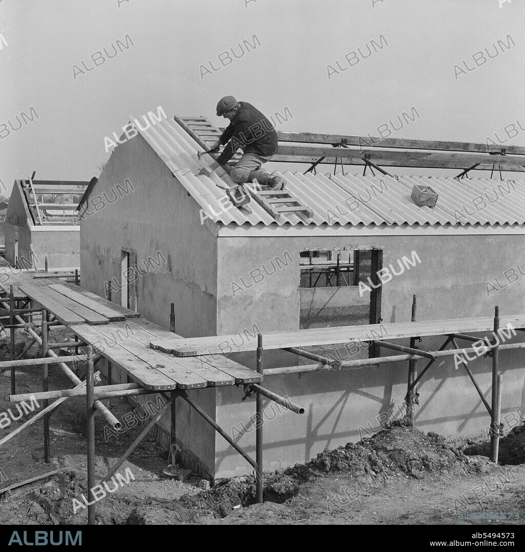JOHN LAING PLC. RAF Gaydon, Gaydon, Stratford-on-Avon, Warwickshire, 11/03/1953. A man fitting corrugated roofing panels onto the roof of a newly constructed building at Gaydon Airfield. Work began on the construction of a new runway at Gaydon Airfield in early 1952. This was followed by a second contract for the construction of more than 100 Easiform and Air Ministry buildings, and 23 Nissen huts.