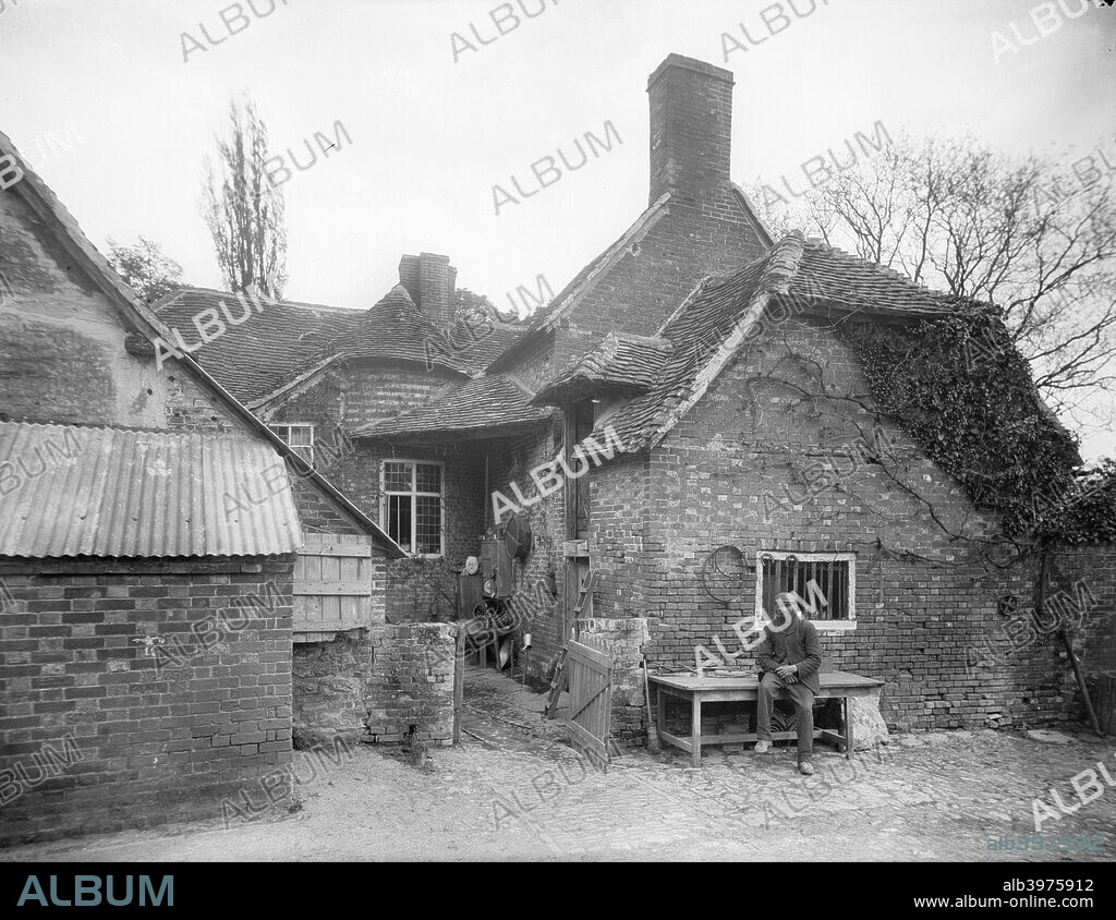Taylors Farm, Didcot, Oxfordshire, c1860-c1922. The rear of the building, which has a several stage tiled roof, showing one of the inhabitants sitting outside on a bench.