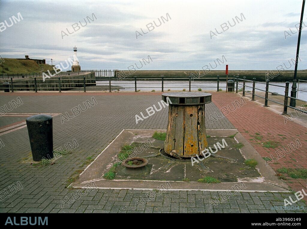 A capstan in the harbour, Maryport, Cumbria, 1999. An old capstan has been reset in the harbour, where it was used for mooring ships. The harbour light can be seen in the distance.