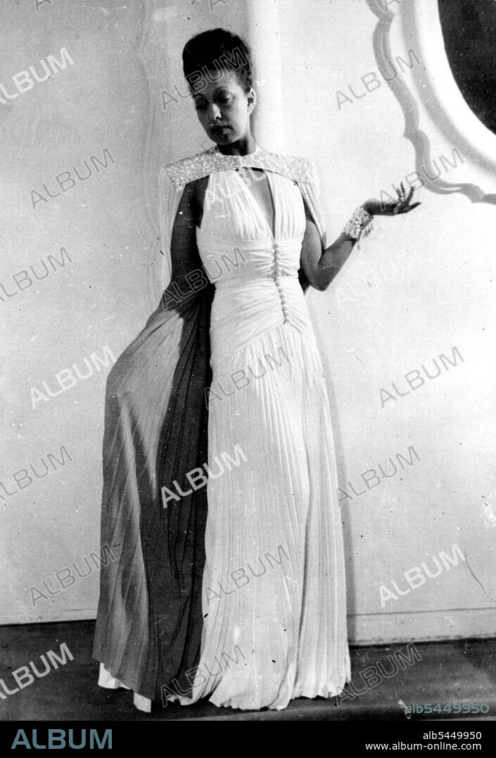 Josephine Baker Gives Private Fashion Show: Josephine Baker wears a Glamourous Russian costume, during the private show at jean dresses - her Parisian dressmaker.This costume has a tunic of white satin, bordered with black velvet Embroidered with Multi-coloured stones. It is high collared in front, like a Russian blouse, leaving the back Bare to the waist. Beneath the flared tunic is worn a long velvet skirt, with sweeping train. Miss Josephine Baker, coloured star or the old Folies Bergeres, and shining light or Frency cabaret, gave a private display in Paris.recently, of the gowns and hats which she will wear when she goes on tour with E.N.S.A., shortly. Miss Baker, who is now in the French Air Force has worked for E.N.S.A., in the middle east played for the troops in Brussels, and may Entertain at army camps in Britain. March 13, 1945. (Photo by Associated Press Photo).