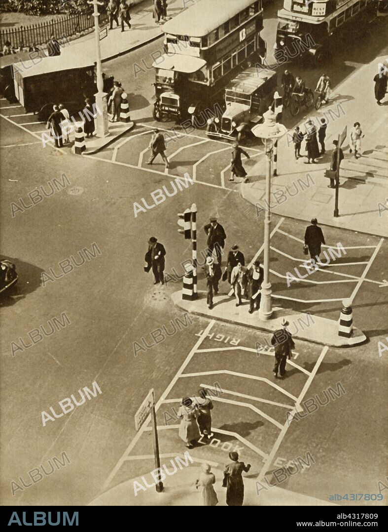 Traffic and pedestrians in Trafalgar Square, London, 1935. 'The last word in traffic control: Belisha Beacons, traffic lights, pedestrian safety lanes, and now - the 30 mph limit in built-up areas'. From "The Silver Jubilee Book - The Story of 25 Eventful Years in Pictures". [Odhams Press Ltd., London, 1935].