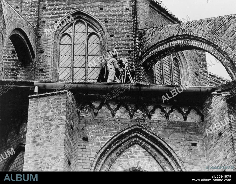 WALTER HEGE. Hege, Walter Photographer 1893-1955.-Filming of documentary "Auf den Spuren der Hanse" (On the tracks of the Hanseatic League): W.camera on roof o.t. ambulatory o.t. Marienkirche in Wismar.-Photo, c. 1930.