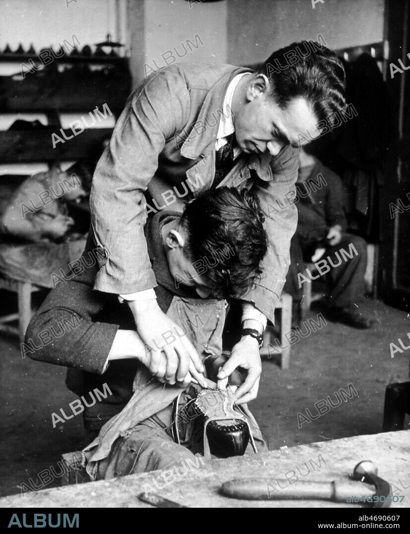 Ecole de cordonnerie de Romans. Le moniteur montre a un apprenti comment coudre une semelle. Photographie d'actualite prise le 26/11/1943. Credit : Collection KHARBINE-TAPABOR.