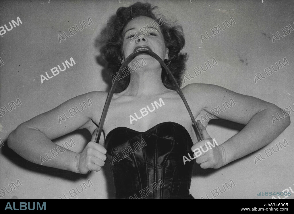 Britain's Strong-Arm Girl -- Miss Joan Rhodes shows how she bends a steel bar with her teeth, demonstrating the tremendous power of her jaw and neck muscles.Probably the strongest girl in Britain to-day is Miss Joan Rhodes, who recently amazed "viewers" with her feats of strength before the television cameras of the B.B.C.Miss Rhodes thinks nothing of tearing thick telephone directories in half with her hands or bending steel bars with her teeth, besides lifting two or three times her own weight.Joan is just "naturally strong" and apart from ordinary sports such as swimming, tennis etc, has never had any special physical training.  March 14, 1950. (Photo by Sport & General Press Agency, Limited).