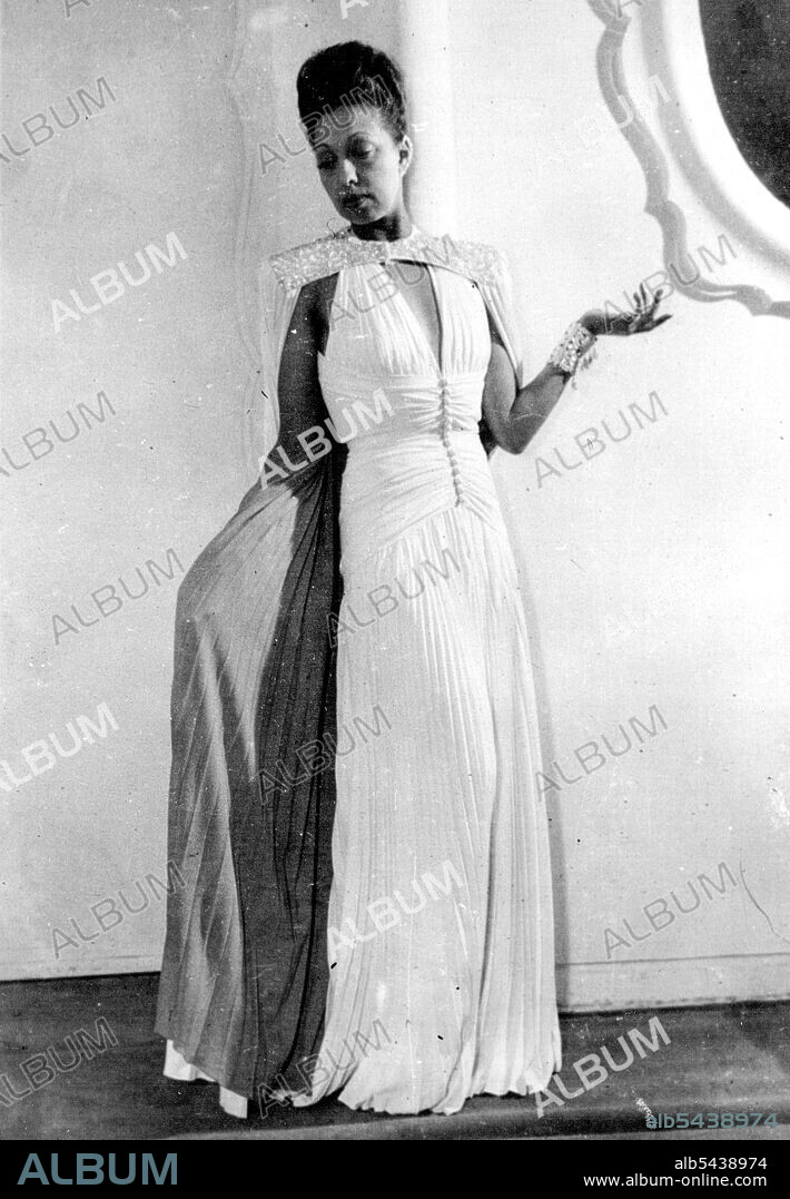 Josephine Baker Gives Private Fashion Show: Josephine Baker wears a Glamourous Russian costume, during the private show at jean dresses - her Parisian dressmaker. This costume has a tunic of white satin, bordered with black velvet Embroidered with Multi-coloured stones. It is high collared in front, like a Russian blouse, leaving the back Bare to the waist. Beneath the flared tunic is worn a long velvet skirt, with sweeping train. Miss Josephine Baker, coloured star or the old Folies Bergeres,.
