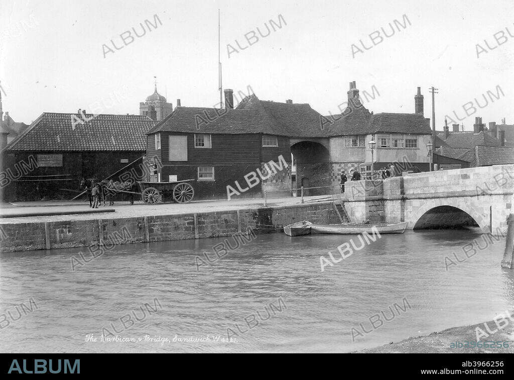The Barbican, Sandwich, Kent, 1890-1910. The river at Sandwich looking towards the north side of the Barbican and the Bridge, with a horse-drawn vehicle on the opposite bank. The Barbican contains 16th-century rounded chequered bastions and was adapted into a tollhouse in the 20th century.