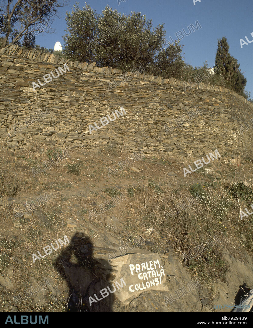 VALLA DE PIEDRA QUE RODEA LA CASA DE DALI-GRAFITI EN CATALAN.