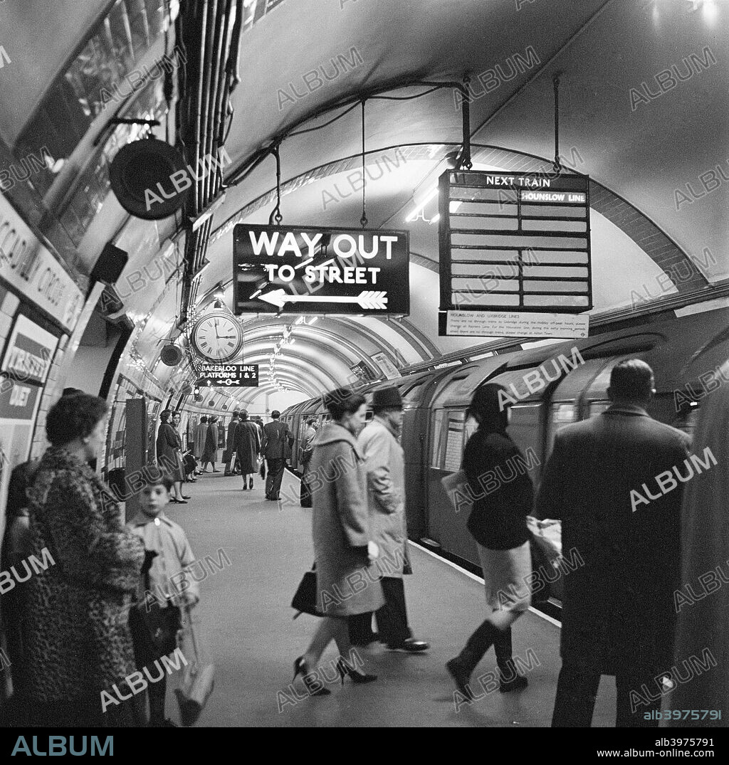 Piccadilly Circus Station, London, 1960-1965. Platform at Piccadilly Circus underground station showing people entering a Hounslow Line train, and the 'Way Out' sign above.