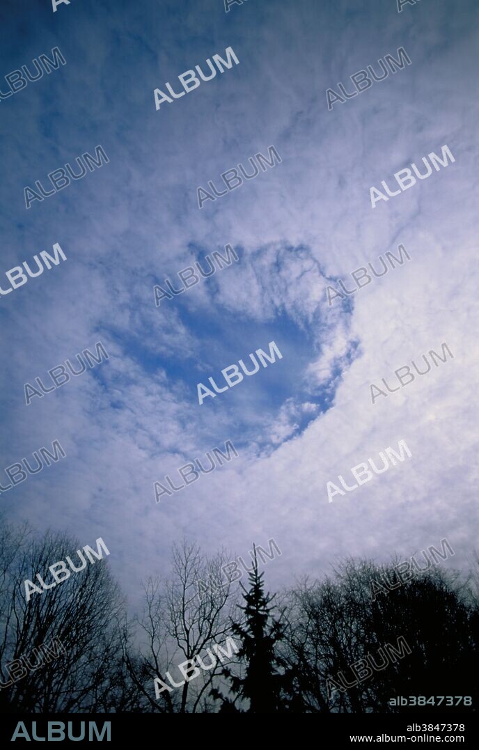"Fallstreak" hole in altocumulus clouds. This phenomena occurs when the super-cooled water droplets that make-up the cloud freeze, often as the result of an aircraft passing through the cloud. The frozen particles eventually grow to fallout size and descend, thus the name "fallstreak".
