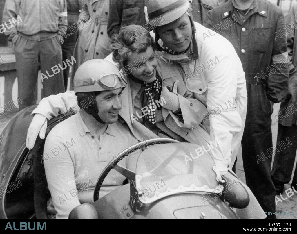 Alberto Ascari in a Ferrari, 1953. Being photographed with a female fan and a young driver. Enzo Ferrari signed Ascari up in 1949, and he won many races for Ferrari between 1950 and 1952. He was World Champion in 1952 and 1953. In 1952 he won every Grand Prix, and didn't lose a race until the middle of 1953. He performed the unrepeated feat of winning nine straight Grands Prix.