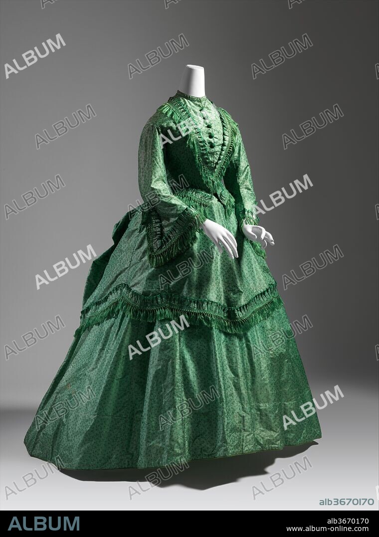 Dress. Culture: British. Date: ca. 1870.
By 1866 fashion had decreed that the fullness of the skirt hsould be gathered up somewhat at the back, and that an overskirt should be added to the full skirt. In 1868 the great expanse of the skirt narrowed considerably  at the side, giving a much straighter silhouette in front; the fullness now moved to center back, where the primary shaping was provided by the bustle.