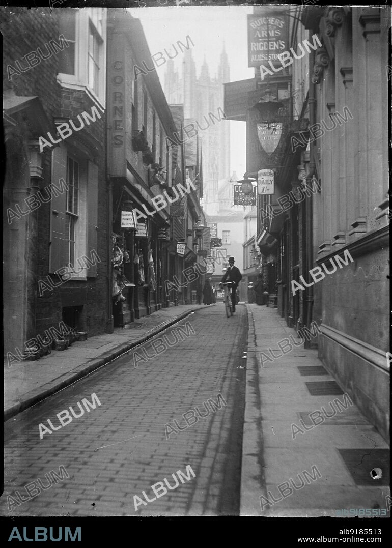KATHERINE JEAN MACFEE. Butchery Lane, Canterbury, Kent, 1904. Looking along Butchery Lane towards the tower of Canterbury Cathedral, showing meat carcasses hanging outside a butcher's shop and a man cycling along the road.