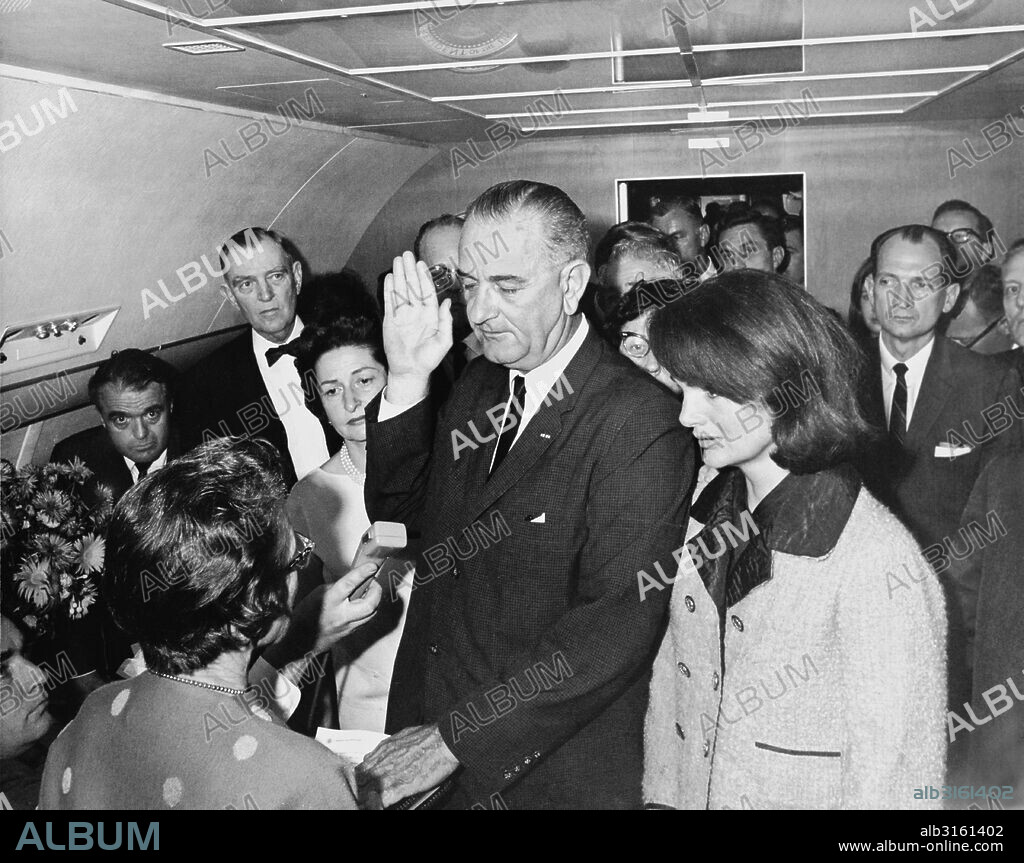 Dallas, Texas: November 22, 1963 Lyndon B. Johnson taking the oath of office on Air Force One at Love Field Airport two hours and eight minutes after the assassination of John F. Kennedy. L-R: Mac Kilduff (holding dictating machine), Judge Sarah T. Hughes, Jack Valenti, Congressman Albert Thomas, Marie Fehmer (behind Thomas), First Lady Lady Bird Johnson, Dallas Police Chief Jesse Curry, President Lyndon B. Johnson, Evelyn Lincoln (eyeglasses only visible above LBJ's shoulder), Congressman Homer Thornberry (in shadow, partially obscured by LBJ), Roy Kellerman (partially obscured by Thornberry), Lem Johns (partially obscured by Mrs. Kennedy), former First Lady Jacqueline Kennedy, Pamela Tunure (behind Brooks), Congressman jack Brooks, Bill Moyers (mostly obscured by Brooks).