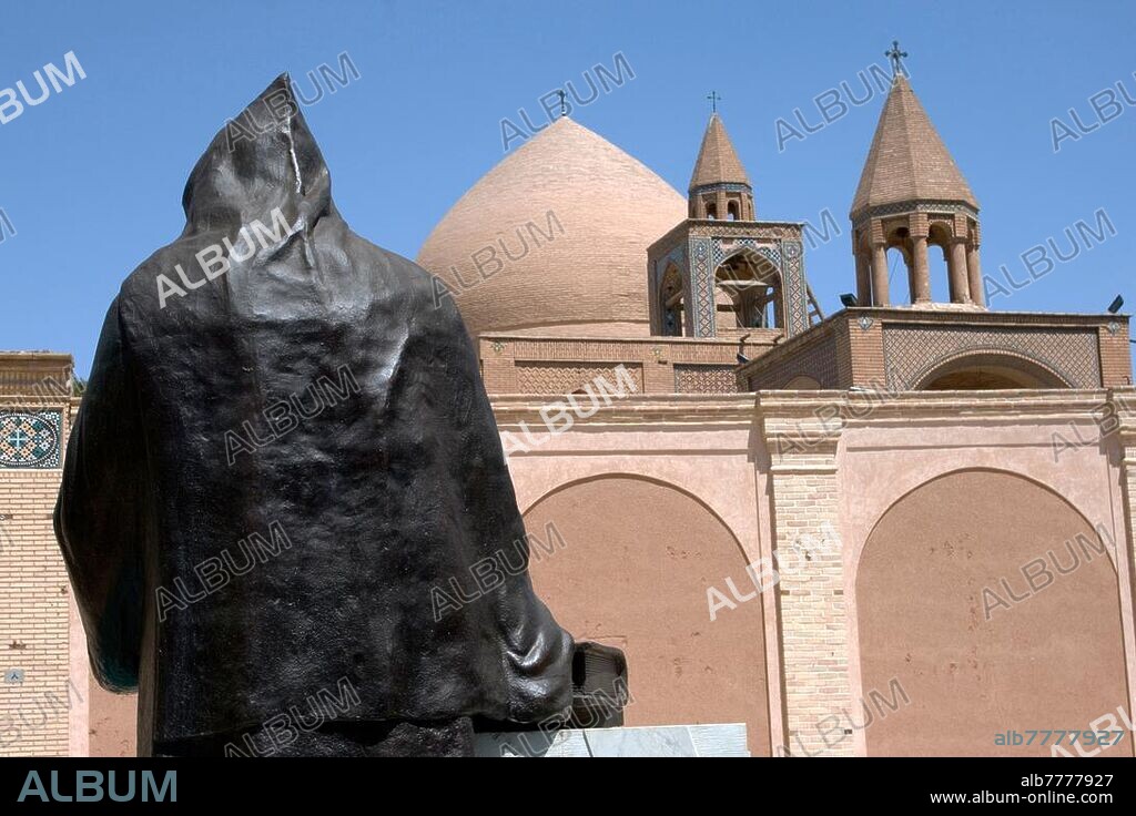 Iran, Isfahan City, forecourt of the Vank Cathedral (Surp Amenaprgich Vank) in the Christian Armenian district of Djolfa (Jolfa): bronze sculpture (rear view) of the Archbishop Khachatour Kesaratsi (around 1636) erected in 2007 against the backdrop of the Vank Cathedral, built 1606 - 1655.  Archbishop in cowl and with bible.  opened the first printing house and publishing house in Iran in 1636. To the district of Djolfa (Christian Armenian Quarter): View over the main dome and bell tower of the so-called Vank Cathedral.