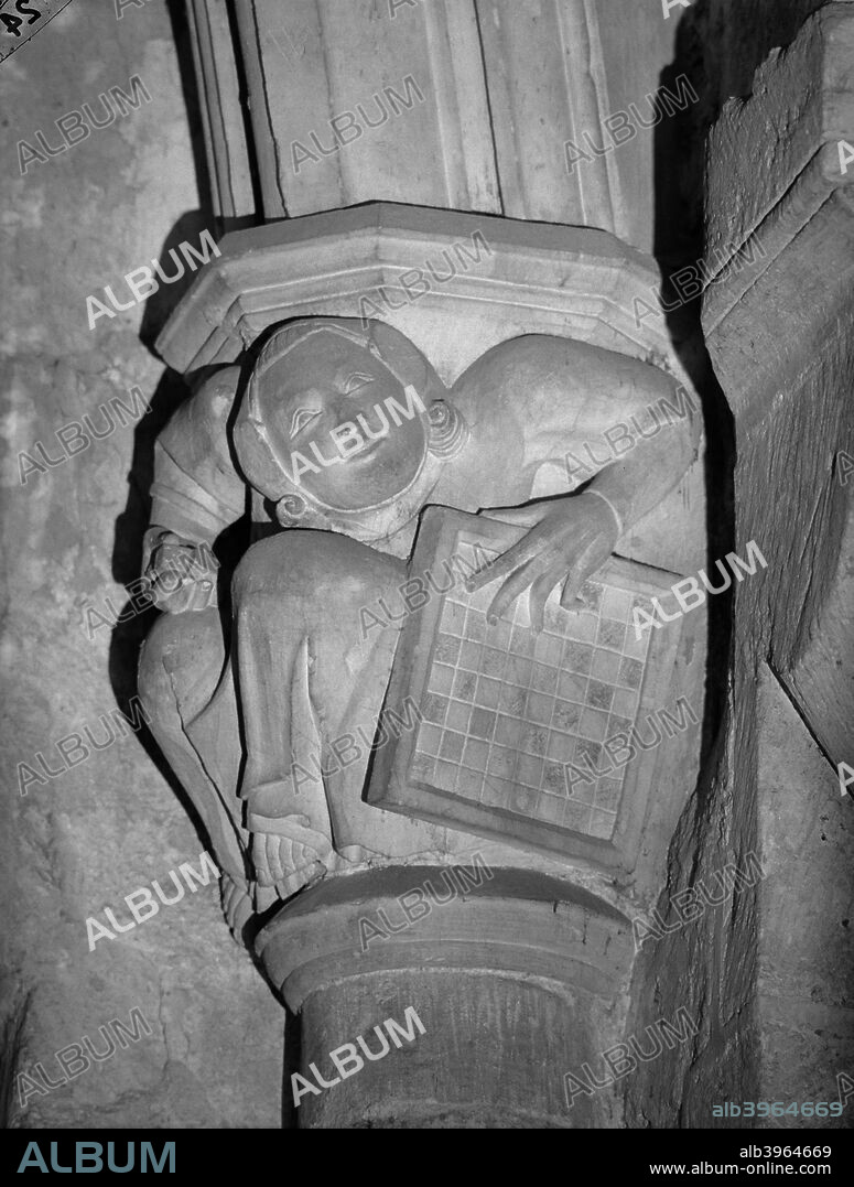 Carved corbel, Winchester Cathedral, The Close, Winchester, Hampshire, 1931. A corbel depicting a figure holding a chess board and dice, in the north transept.