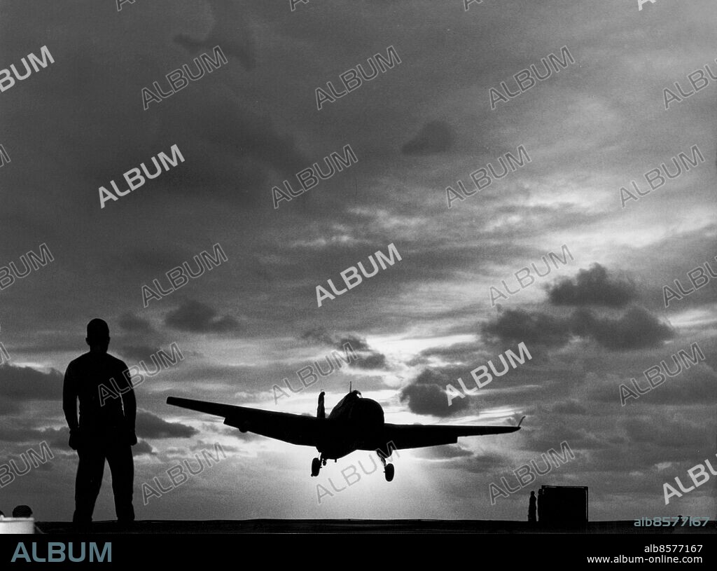 Orig. bildtext... HOME TO ROOST AT SUNDOWN Korea.........Ensign Jack Radican, of VS 892, a navy scout squadron, brings his plane in for a landing on the flight deck of the escort carrier USS Rendova as the sun goes down from a troubled sky over Korean waters. It was the 9,000th landing on the Rendova, which has been operating in Korean waters since last August, giving support to U.N. ground forces with the famed marine Devilcat squadron on board. 12.7.51. Orig. bildtext... NIGHT LANDING-making the 9,000th landing onboard the escort aircraft carrier USS Rendova (CVE114). Ens, Jack Radican of VS 892, a navy scout squadron, settles down on the flight deck of the carrier. The Rendova has been operating off the coast of Korea since last Aug., giving support to United Nations ground forces with the famed marine Devilcat squadron on board. The Rendova is commanded by Capt. Evan E. Fickling, USN, of South Carolina. Orig. bildtext... Ett plan landar på amerikanska hangarfartyget Rendova som opererar i koreanska farvatten. Anm. Solnedgång Siluetter Landning Himmel Precision CD643 persons: JADICAN RADICAN* sites: KOREA;USA*.