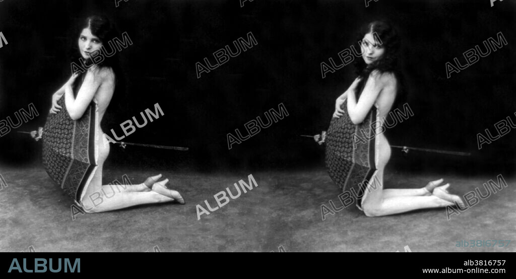 Entitled: "A Galaxy of art" showing a nude woman kneeling and holding open umbrella in front of herself. Stereograph card photographed by Exhibit Supply Company, 1928. RisquÃ© photography is material that is slightly indecent or liable to shock, especially as sexually suggestive. These mildly provocative stereographs were marketed for parlor use in the early 20th century. Used with a stereoscope, the side-by-side images would render in 3D.y-side images would render in 3D.