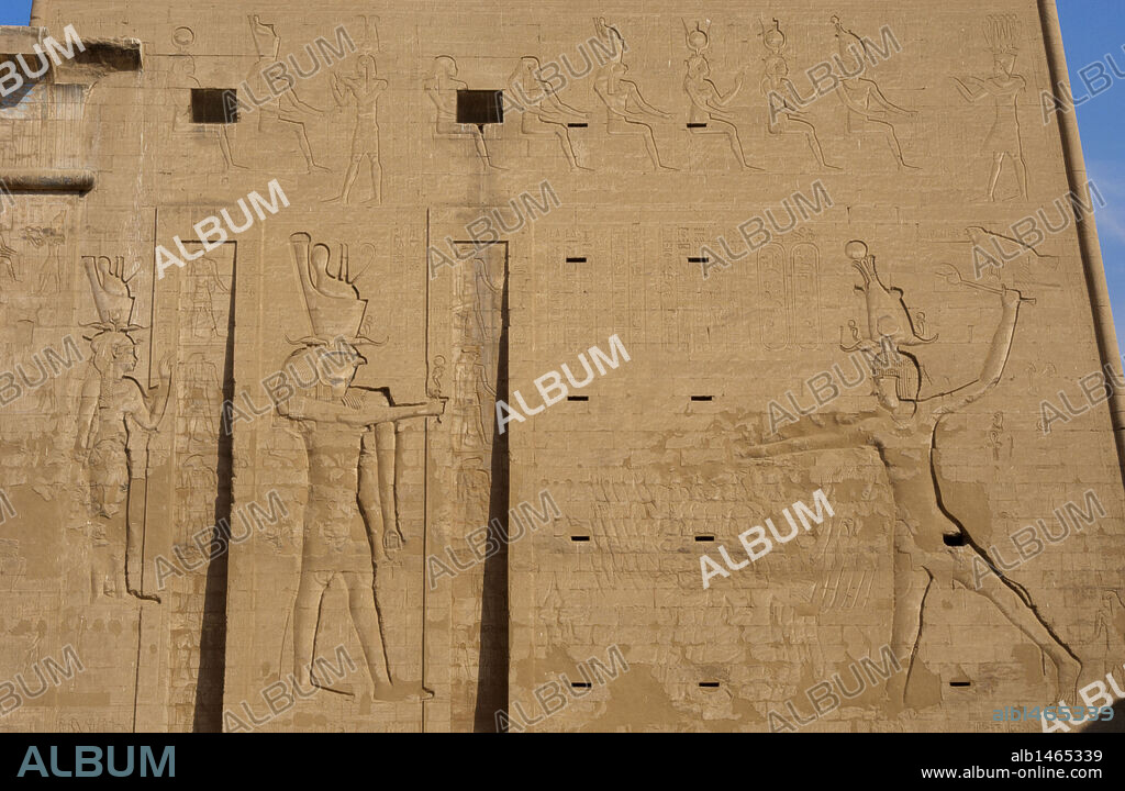 ARTE EGIPCIO. TEMPLO DE HORUS. EDFU. Decoración en relieves del PILON de entrada, en el cual se encuentran representados el faraón PTOLOMEO XII NEO DIONISO sacrificando prisioneros ante el dios HORUS (cabeza de halcón) y HATHOR (figura femenina). EDFU. Egipto.
