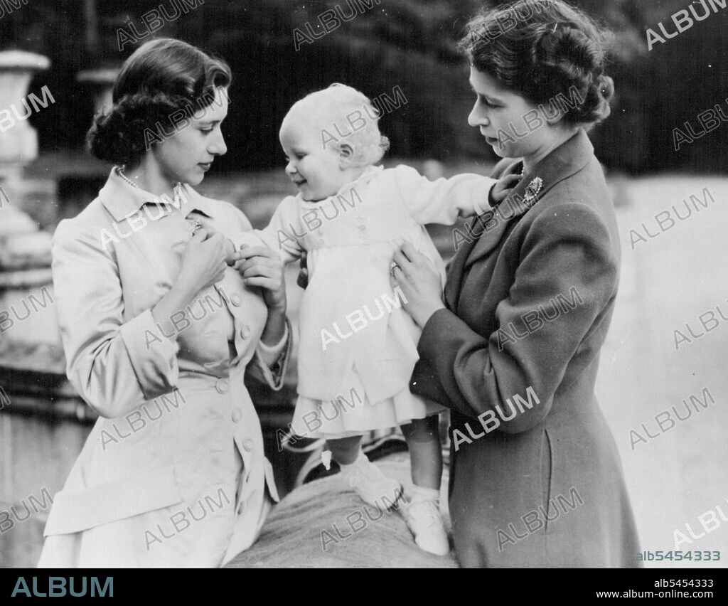 The Royal Family At Balmoral : A charming study of the Royal sisters taken during one of these happy family gatherings. It shows Princess Elizabeth (right) and Princess Margaret help balance baby Princess Anne on a balustrade in the castle grounds. Like all babies, Princess Anne loves sparkling things and plays delightedly with Princess Margaret's brooch. The King and Queen and Princess Margaret who are in residence at Balmoral Castle, Scotland, are being paid frequent visits by Princess Elizabeth and the Duke of Edinburgh, staying at nearby Birkhall. Royal approval has been given for the publication of these delightful photographs made in the castle grounds by Mr. James Reid, a Ballater photographer. August 21, 1951. (Photo by Paul Popper).