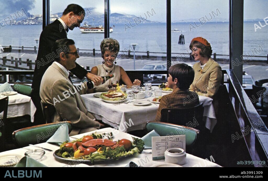 The Franciscan Restaurant, Fisherman's Wharf, San Francisco, California, USA, 1965. Scene showing a family dining at the Franciscan Restaurant. The waiter pours wine and a gourmet meal is in the foreground. There is a spectacular view of San Francisco Bay from the window.