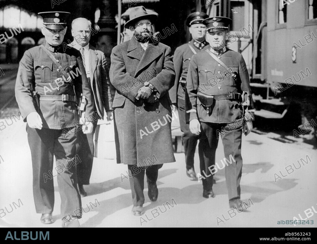 Orig. bildtext... HUNGARIAN MASS MURDERER SENT HOME. Handcuffed and heavily guarded by police, Silvester Matuska, tall, bearded, forty-two year old Hungarian found guilty of mass murder in his native land, was put on a train at Vienna to be sent back to Budapest. Matuska was tried and sentenced to death in connection with the wrecking of the Budapest-Vienna express at Bia Torbagy in 1931, but has so far managed to avoid the carrying out of the sentence. PHOTO SHOWS: Silvester Matuska handcuffed and escorted by a strong guard of police as he walked to the train at Vienna. September 30th 1936 Anm. Sylvester Matuska, född i Ungern 1892, försvunnen 1945. 13 september 1931 sprängde han järnvägsbron nära Biatorbagy i Ungern och nattåget Budapest-Wien störtade 25 meter. 24 personer omkom, 14 skadades svårt och flera fick lättare skador. Fångar Handbojor Handfängsel Massmördare På rad Skägg CD627 persons: SYLVESTER MATUSKA sites: ÖSTERRIKE;UNGERN*;WIEN.