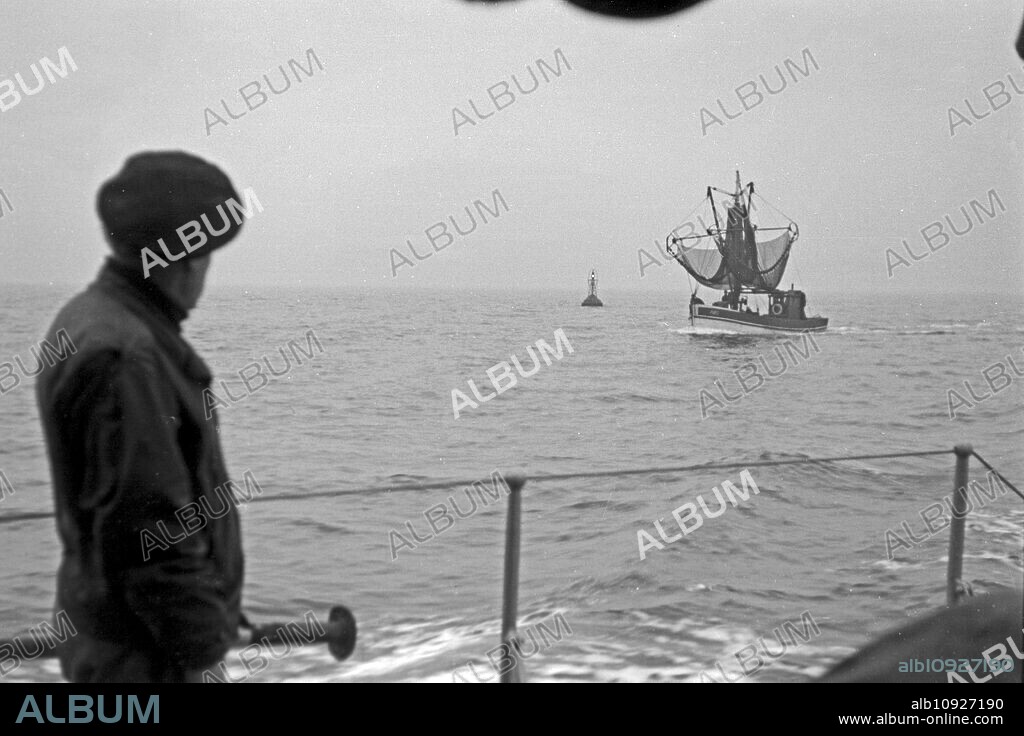 A dockworker seeing a fishing boat leaving Emden harbor for fishing, Lower Saxony, Germany 1950.