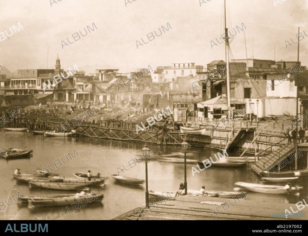 Fire damage on the wharf. People stand amidst the rubble; in foreground, boats and a pier.