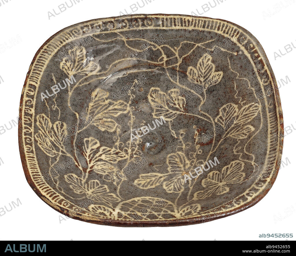 Plate with grapevines, trellis, and geometric design, late 16th century, Unknown Japanese, 2 3/4 × 11 3/16 × 10 9/16 in. (6.99 × 28.42 × 26.83 cm), Mino ware, Nezumi-Shino type; stoneware with underglaze iron oxide, Japan, 16th century, Mino ware, Nezumi Shino type; Formal tea gatherings are accompanied by kaiseki, multicourse communal meals at which dishes would be served on plates like this one, which was created by a potter in the Mino region of central Japan. Mino potters in the late 1500s produced a wide variety of innovative ceramic styles in quick succession, with each style swiftly arousing interest, but then just as quickly dying outwares that included the now celebrated Black Seto, Yellow Seto, Oribe, and Shino styles. This plate represents a substyle of Shino ware known as Nezumi, or 'mouse-gray' Shino. Potters created these wares by applying a coat of iron-rich slip (liquid clay) to the formed vessel, allowing it to dry, and then using a sharp tool to etch a design into the coating, revealing the white clay below. This and other Mino vessels from the late 1500s were fired in partially underground kilns known as an gama.