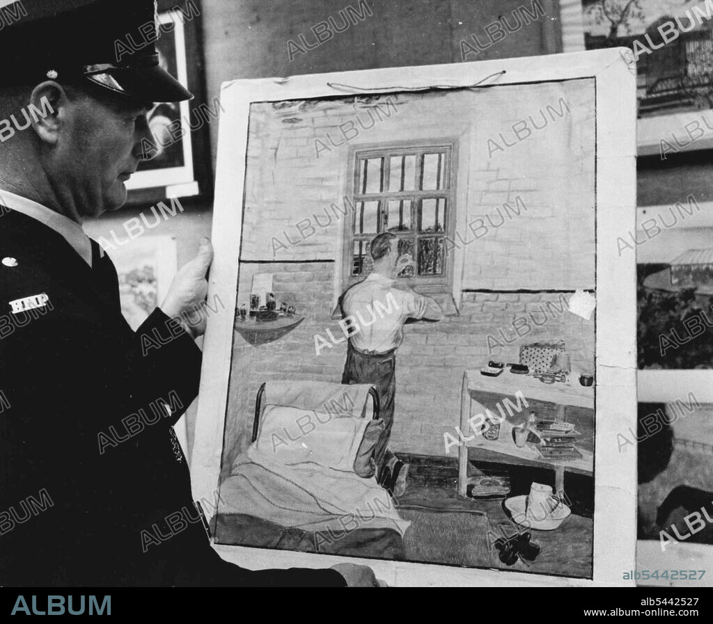 They Think Of The Small things -- A 29-year-old salesman painted this picture being explained by Wandsworth Prison officer J.Shaw. For the preview of a big art exhibition in London this afternoon, not one of the artists whose pictures hung on the walls was present. All of them were anxious to know how the public and the experts were reacting to their skill. but this will have to be reported to them. For all the artists are in prison or Borstal. Most have never handled palette or brush before. Their pictures are not for sale. These are on view until a week next Saturday at the Imperial Institute Galleries. South Kensington. They illustrate the thoughts and expressions from prison cells which could not always be put clearly into words. They often show nostalgia for the outside world. July 14, 1952. (Photo by The Evening News).
