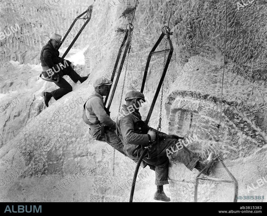 Construction workers hanging by cables with Borglum monitoring the work. John Gutzon de la Mothe Borglum (March 25, 1867 - March 6, 1941) was a Danish-American artist and sculptor famous for creating the monumental presidents' heads at Mount Rushmore, South Dakota; the famous carving on Stone Mountain near Atlanta; and other public works of art. He died in 1941 at the age of 73. Mount Rushmore National Memorial is a sculpture carved into the granite face of Mount Rushmore near Keystone, South Dakota. Sculpted by Borglum and his son, Lincoln Borglum, Mount Rushmore features 60 foot sculptures of the heads of four United States presidents: George Washington, Thomas Jefferson, Theodore Roosevelt, and Abraham Lincoln. Construction on the memorial began in 1927, and the presidents' faces were completed between 1934 and 1939. Although the initial concept called for each president to be depicted from head to waist, lack of funding forced construction to end in late October 1941. Mount Rushmore has become an iconic symbol of the United States, and attracts over three million visitors annually. Photographed by Charles D'Emery, undated.
