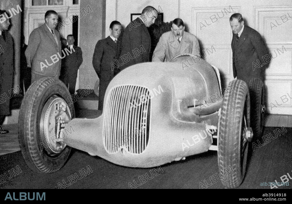 'Mercedes Benz racing car built on suggestion of the Führer', Germany, 1936. German Nazi leader Adolf Hitler (1889-1945) looking at one of the famous 'Silver Arrows' which enjoyed great success in motor racing in the 1930s. A print from Adolf Hitler. Bilder aus dem Leben des Führers, Hamburg: Cigaretten/Bilderdienst Hamburg/Bahrenfeld, 1936.