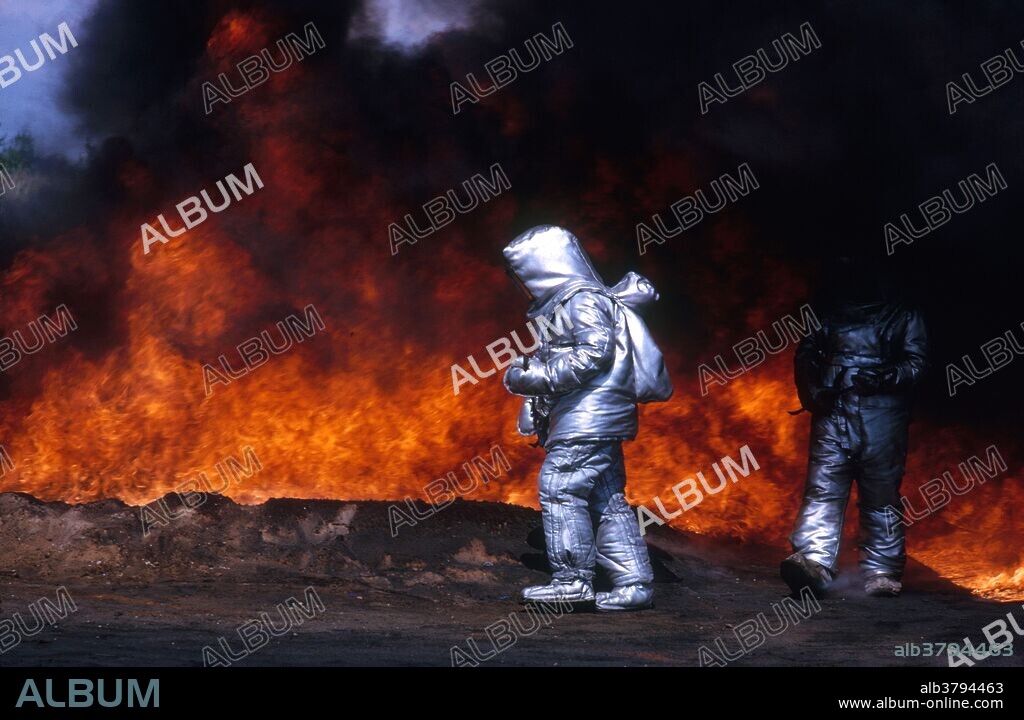 Older image of a man testing out an asbestos firefighting suit in a waste oil fire.