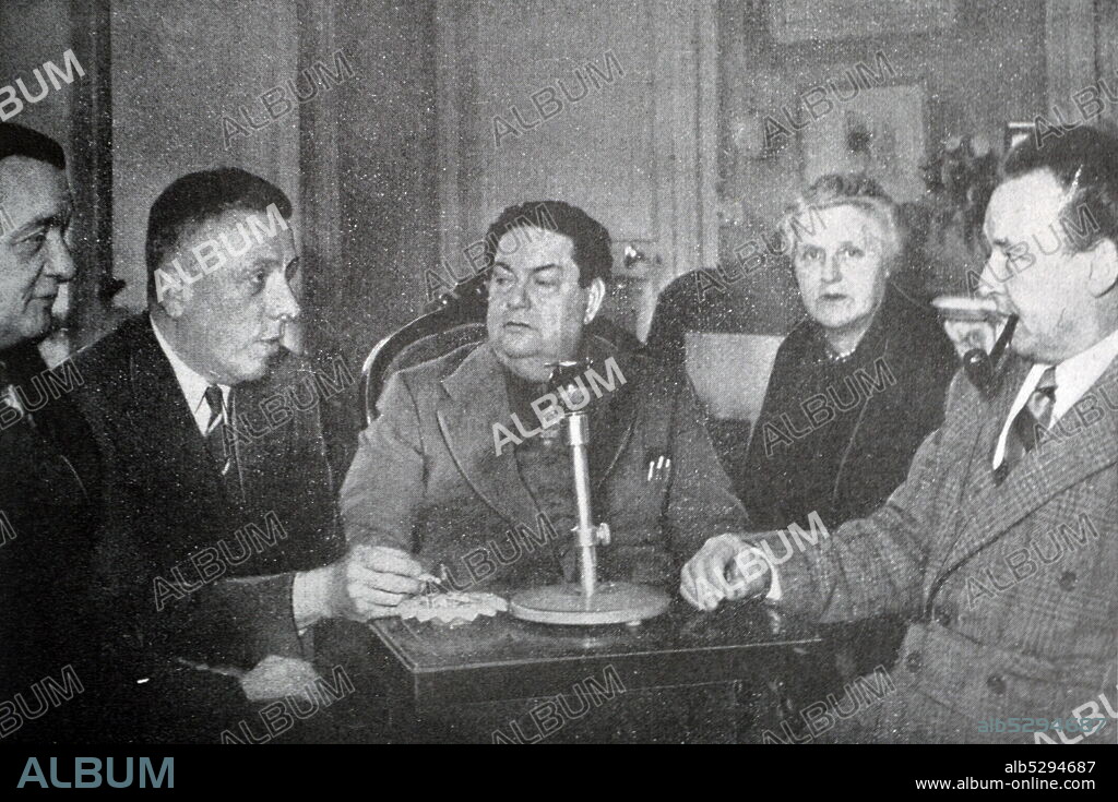 Black and white photograph of Darius Milhaud (1892-1974), French composer, at an evening party with French pianist and teacher Marguerite Long (1874-1966), French composer and pianist Francis Poulenc (1899-1963), French composer Georges Auric (1899-1983), and Swiss composer Arthur Honegger (1892-1955).