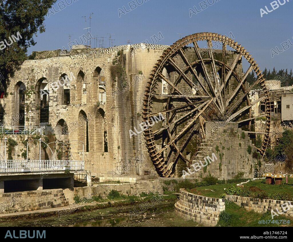 SIRIA. HAMA. Vista general de la NORIA medieval ubicada en uno de los jardines del centro de la ciudad, junto a la ribera del río Orontes. Junto a ella, el ACUEDUCTO, sustentado por elegantes arcadas de piedra, que hacía llegar el agua a las mezquitas y edificios públicos aledaños.