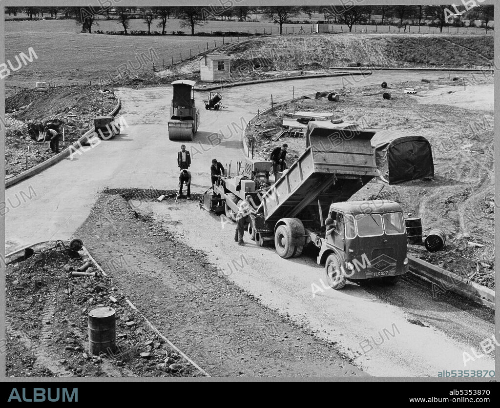 JOHN LAING PLC. A view of the construction of the Birmingham to Preston Motorway (M6), looking down from Structure 369/1 at Junction 16 on Section D of the motorway, showing 'C.B.G.B.C' in progress on the roundabout. The work on the Birmingham to Preston Motorway (M6), between junctions J13 to J16 started in June 1960 and was carried out by John Laing Construction Ltd. Section D was 7 1/2 miles in length between Keele and Barthomley. The 'C.B.G.B.C.' recorded in the album is a reference to the laying of Concrete Bound Granular Base Course.