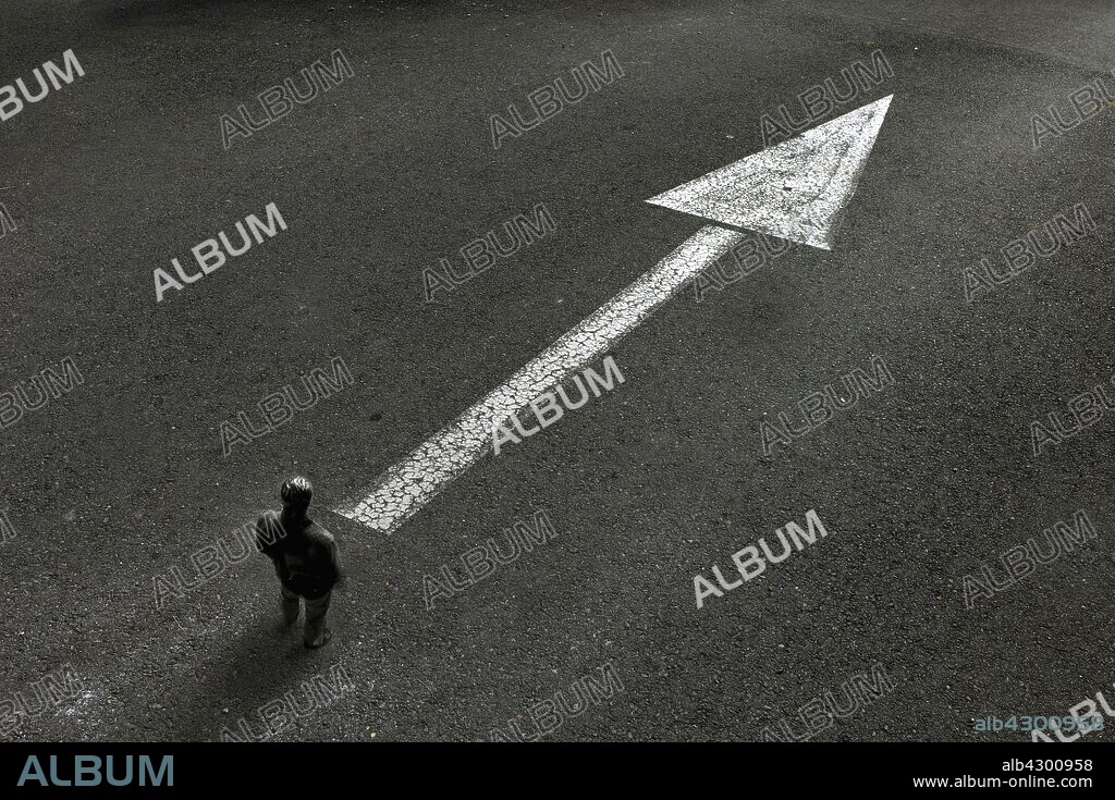 Man standing looking at arrow painted on road pointing the way ahead.