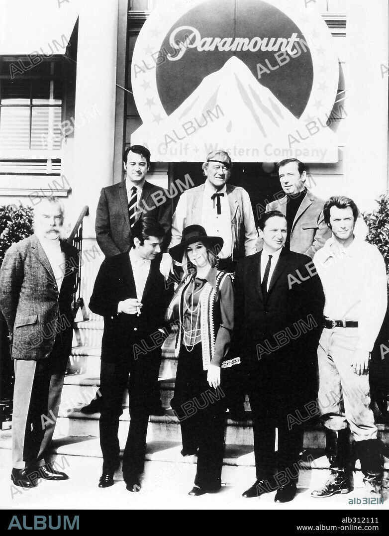 BARBRA STREISAND, CLINT EASTWOOD, JOHN WAYNE, LEE MARVIN, ROBERT EVANS, ROCK HUDSON and YVES MONTAND in FILM HISTORY: PARAMOUNT PICTURES. Cinema stars Rock Hudson, John Wayne, Yves Montand, Lee Marvin, Barbra Streisand and Clint Eastwood pose in front of the Paramount pictures with the producer Robert Evans.